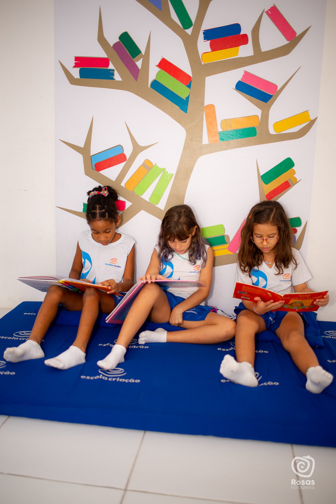 Três crianças lendo livros no cantinho de leitura da Educação Infantil