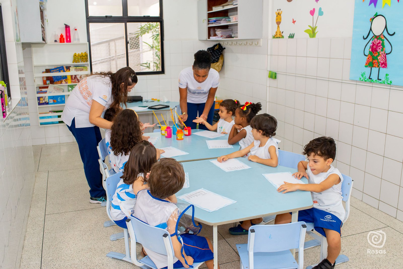 Professora acompanhando crianças pequenas em mesa de atividades