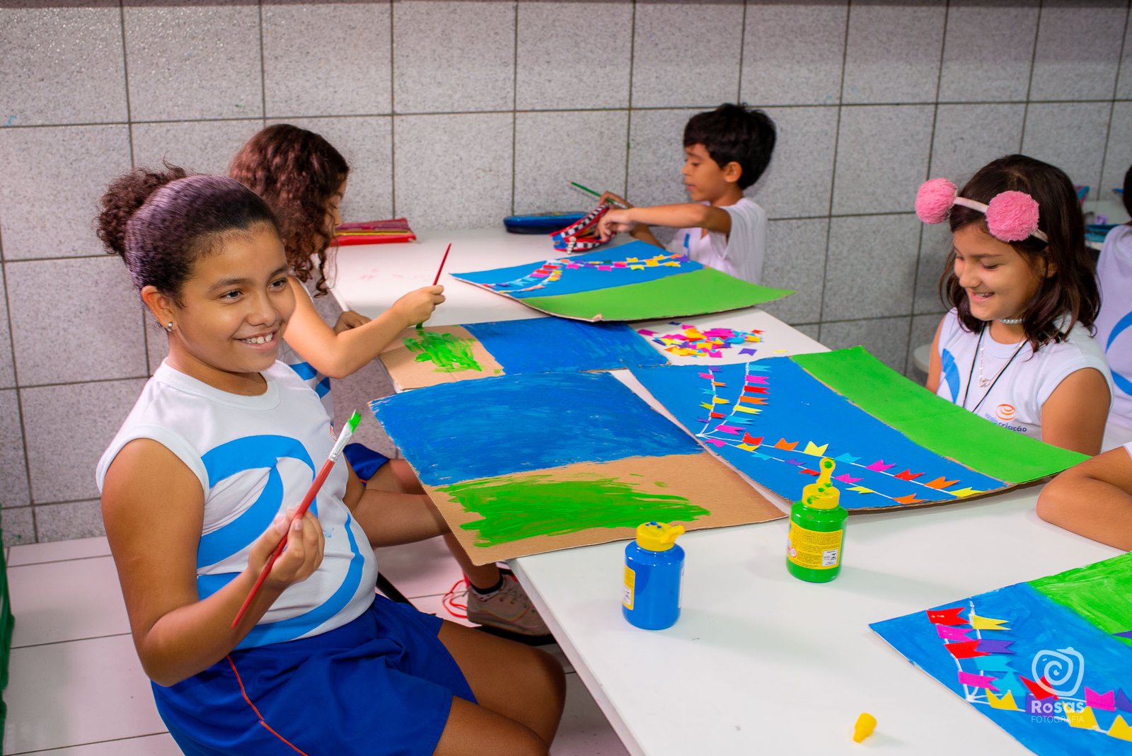 Estudantes pintando com tinta guache em mesa do ateliê de artes