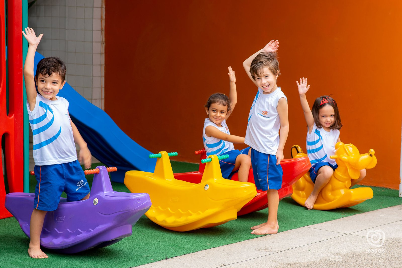 Crianças de braços erguidos no escorregador do playground