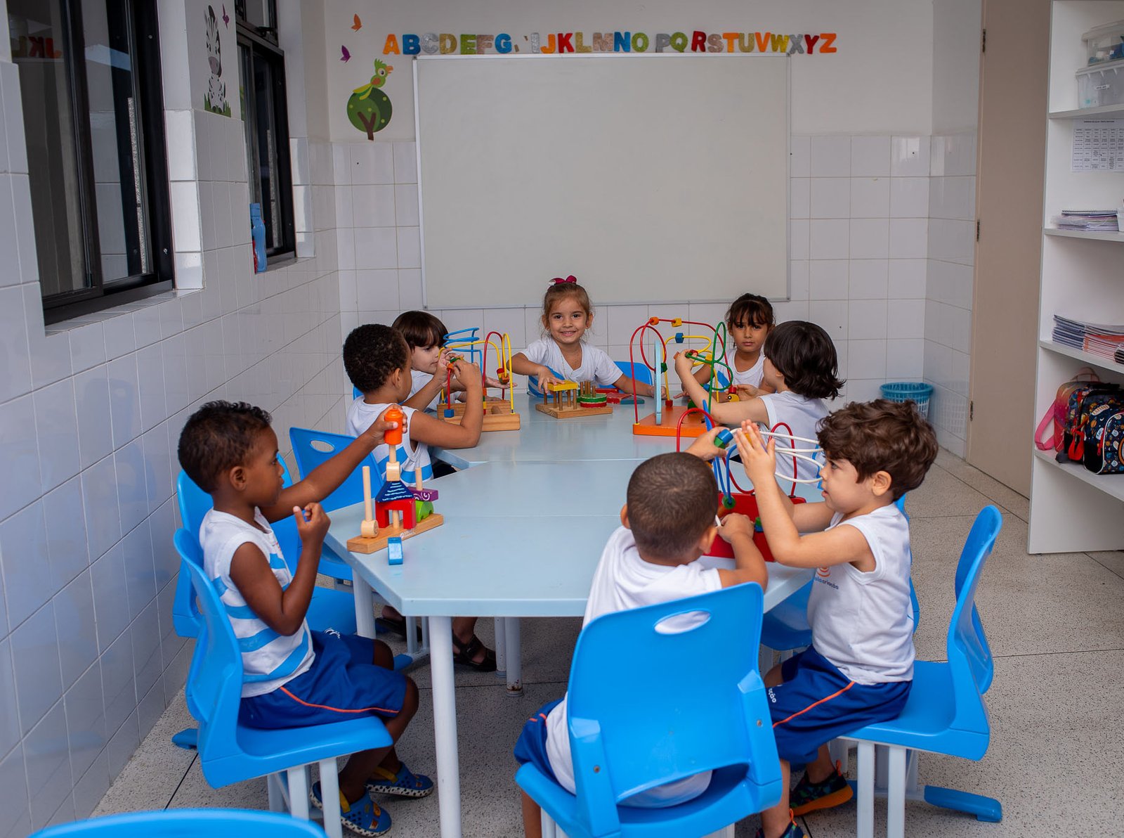 Crianças brincando com jogos educativos em mesa da Educação Infantil